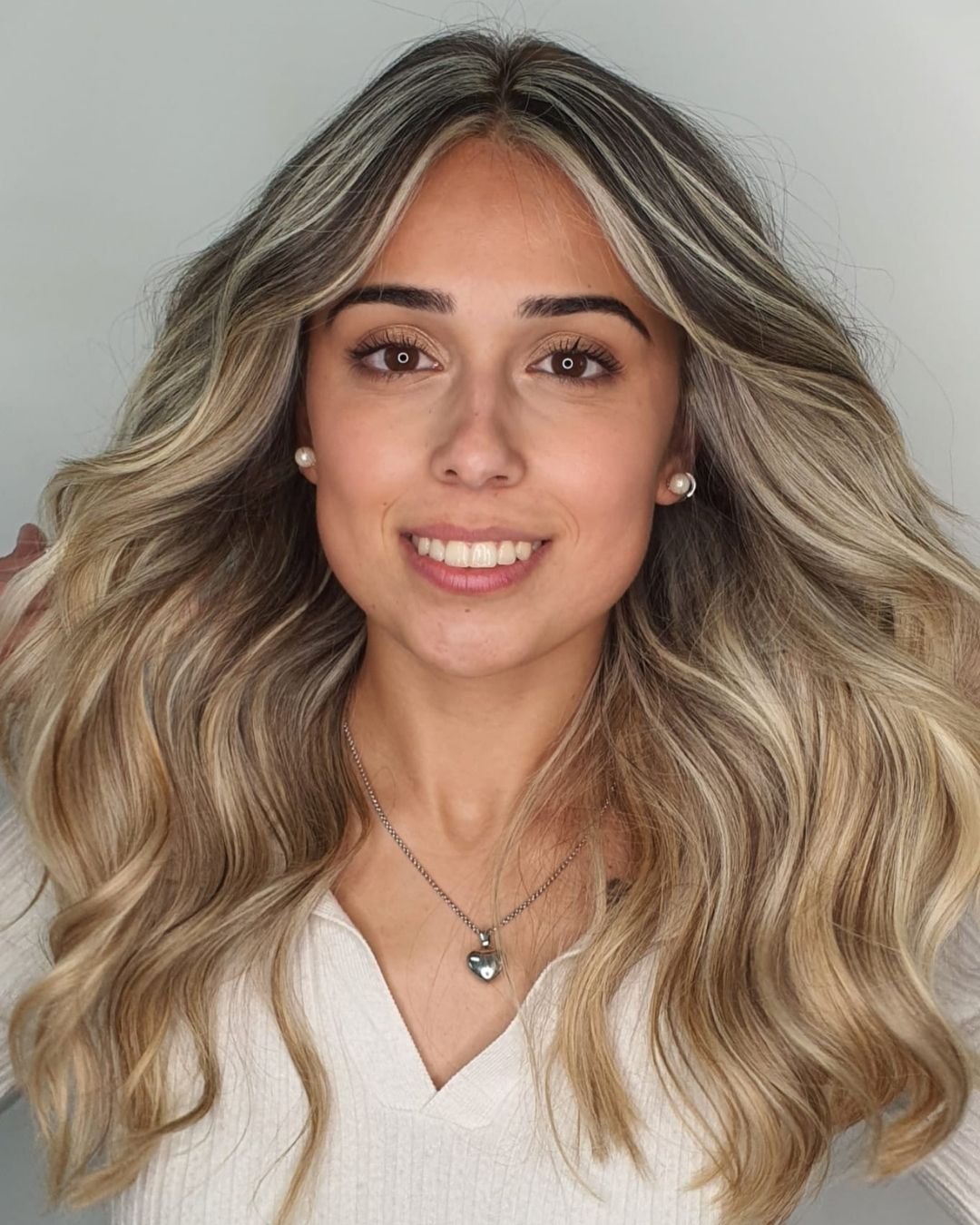 Cliente sorridente com cabelo louro ondulado e raiz esfumada